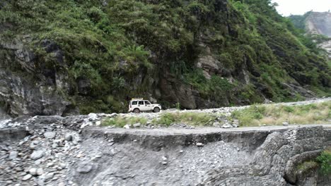 suv offroad car driving tourists on narrow mountain dirt road to jomsom in kali gandaki gorge in central nepal - aerial side tracking