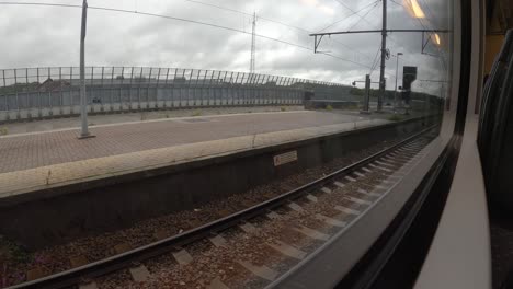 pov shot of platform through train's window which slowly depart from train station