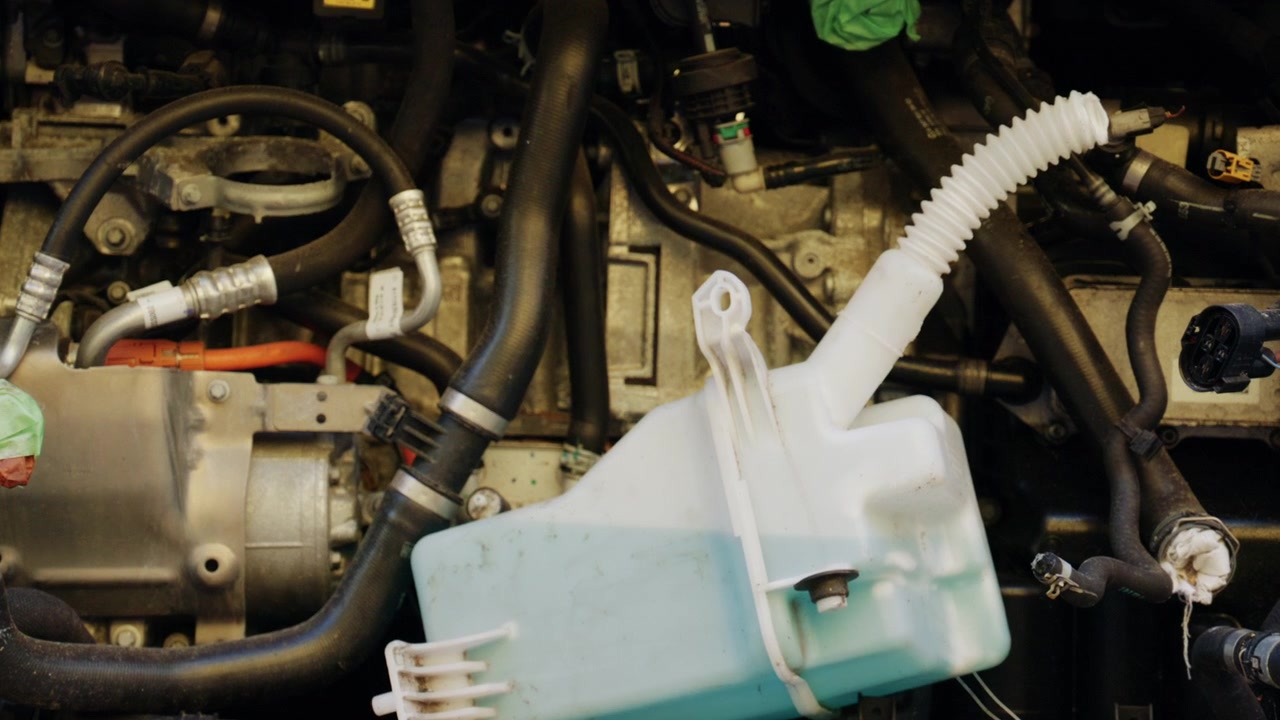 Close up front view of a dismantled car with exposed engine components, hoses, wiring, and missing body panels