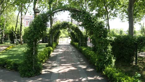 a path lined with trees and arches of vines leading through a park