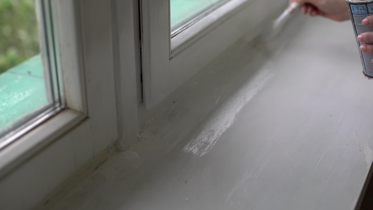 한 여자가 창문의 경사면을  ⁇ 색 페인트로 칠하고, 창문의 구 ⁇ 을  ⁇ 솔로 칠하고, 창문 프레임을  ⁇ 색 페인트의 롤러로 칠합니다.