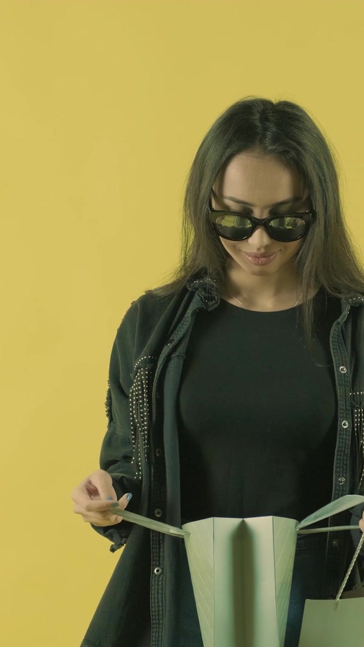Giovane donna che guarda dentro le borse della spesa su sfondo giallo