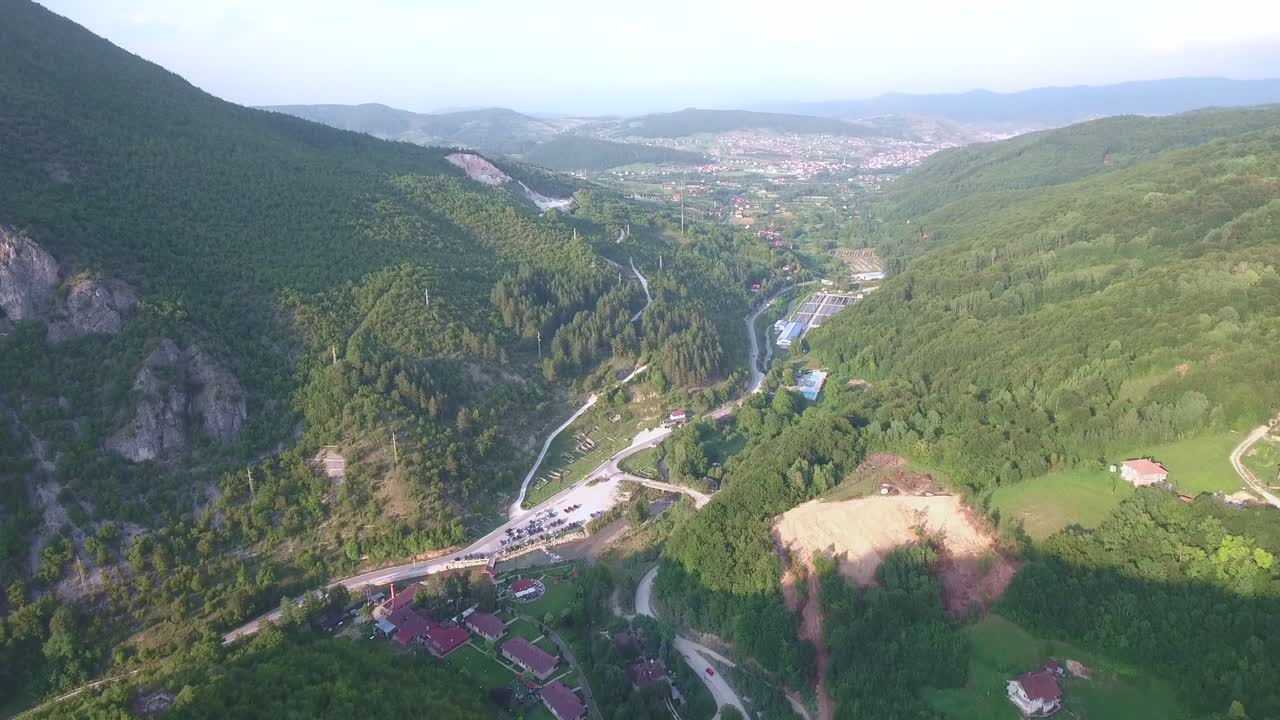 pequeño pueblo en las afueras de novi pazar junto a la montaña con bosques y conducción de automóviles, inclinación aérea hacia adelante