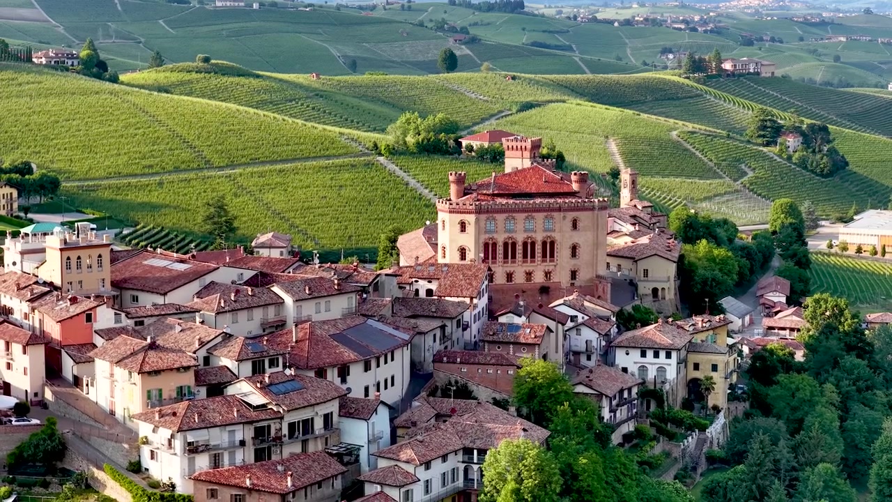 Ripresa con drone cattura il villaggio storico e il castello circondati da dolci colline verdi di vigneti.