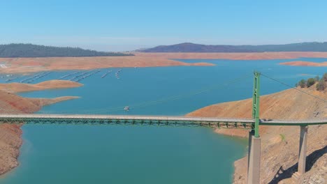 disturbing aerial over drought stricken california lake oroville with low water levels, receding shoreline and large bridge crossing