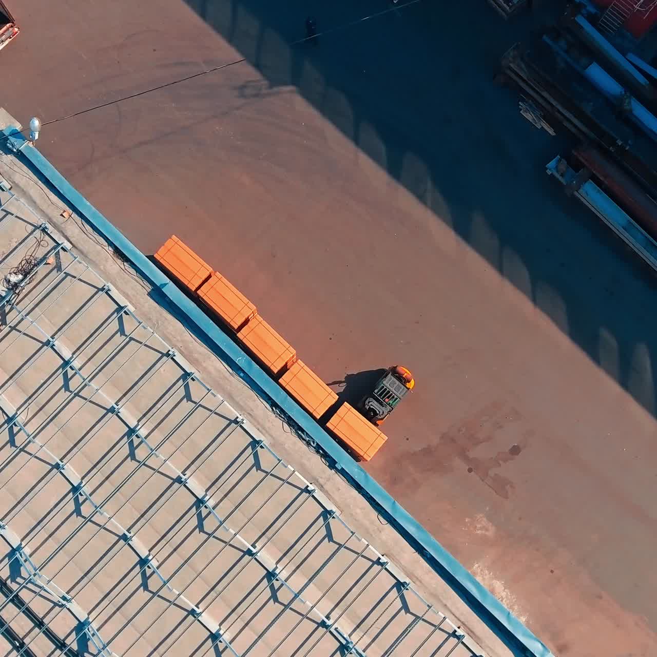 Skid loader unloading boxes from a lorry. Little machine stacking packs near the warehouse wall. View from top