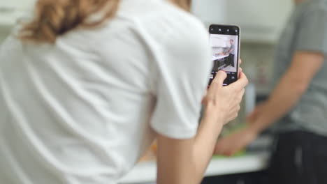 closeup woman hands making mobile videos of male cooking food.