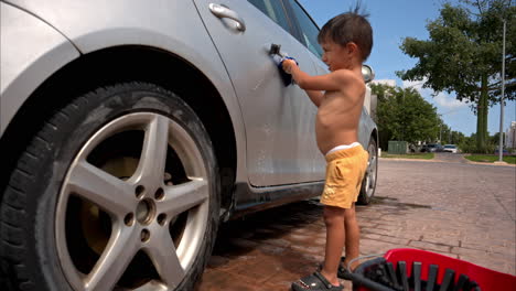 Cámara-Lenta-De-Un-Chico-Latino-Mexicano-Sin-Camisa-Ayudando-A-Sus-Padres-A-Limpiar-El-Auto-Familiar-En-Un-Día-Caluroso-Y-Soleado-Usando-Un-Cepillo-Y-Un-Trapo