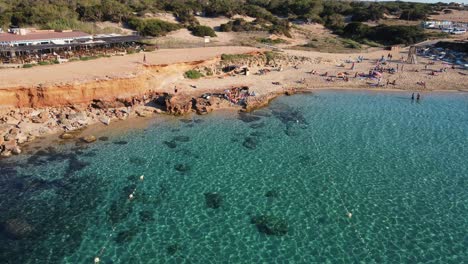 Surfistas-En-La-Playa-De-Cala-Comte,-Retirada-Aérea-De-Ibiza-Para-Revelar-La-Belleza