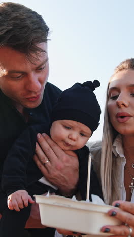 caucasian couple with a newborn blowing a candle on the cake. happy family celebration outdoors. low angle view. vertical video