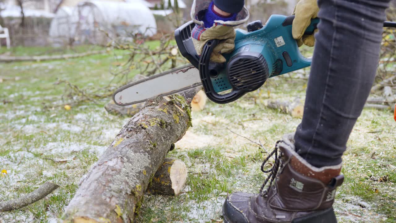 Sawing Apple tree trunk with an electric chainsaw - spring cleaning in garden