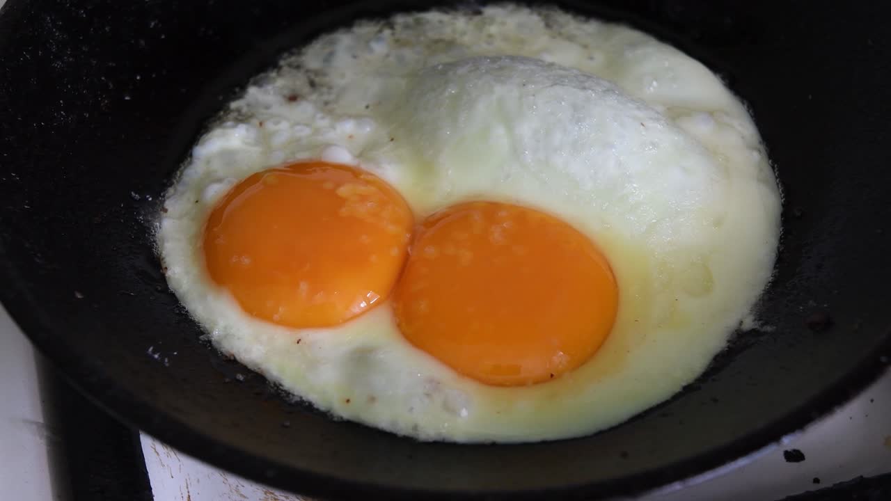 Proses persiapan telur goreng di wajan besi cor.