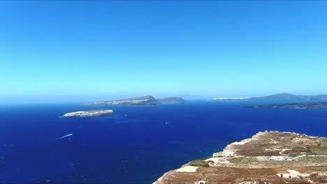 Luft-4k-Blaues-Meer-Und-Himmel-Draufsicht-Auf-Die-Dorfklippe-Mit-Fernem-Segelboot-In-Santorini-Griechenland
