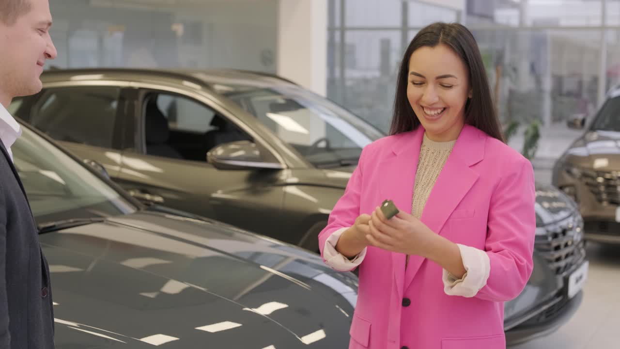 la mano del hombre le da las llaves del coche a la mano de la mujer en el concesionario de automóviles de cerca. el concesionista le da la llave al nuevo propietario en una exposición de automóviles o salón.