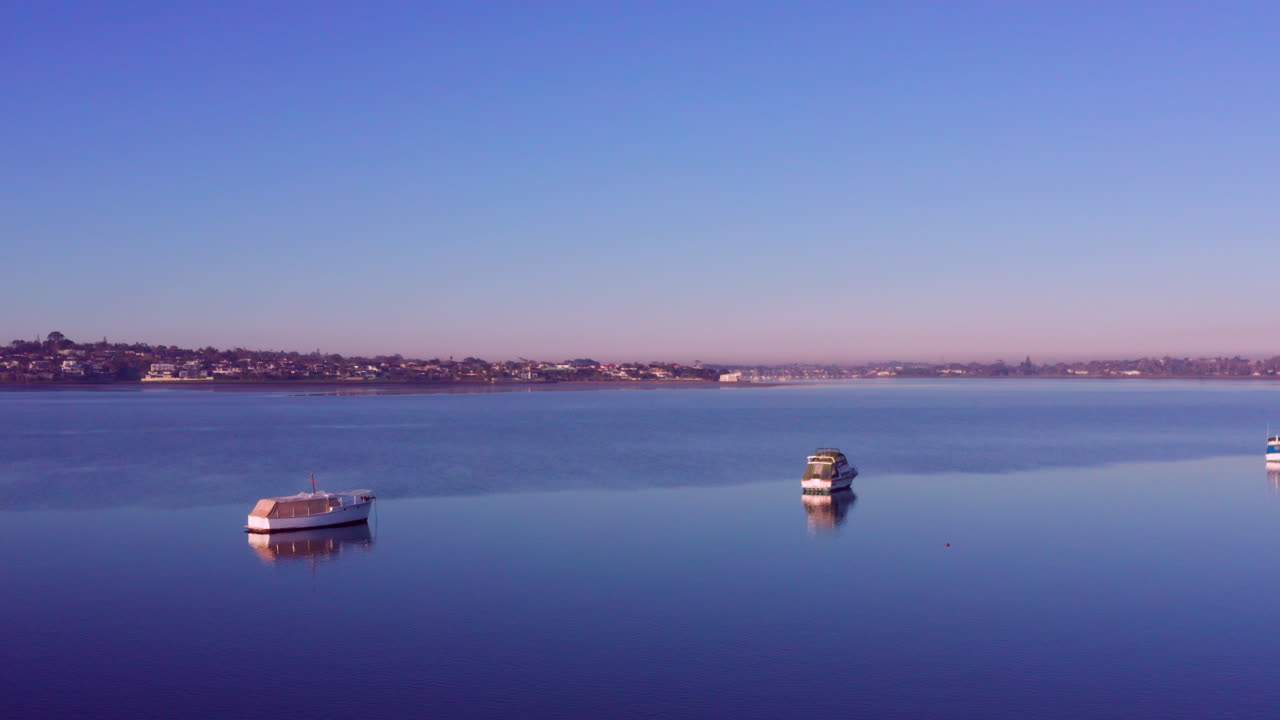 뉴질랜드 오클랜드에서 일출 동안 잔잔한 바다에 정박하고 떠 있는 흰색 범선