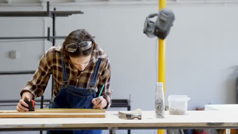 Female-welder-measuring-a-wooden-plank-4k