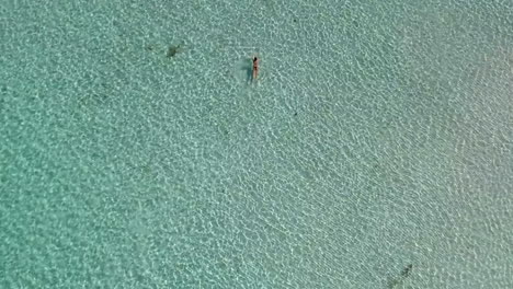 Aerial-shot-of-a-woman-swimming-in-shallow-crystal-clear-waters-on-a-sandy-beach-at-a-holiday-resort