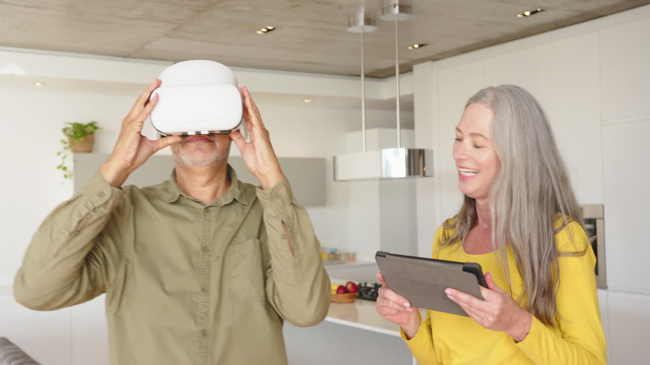 Using VR headset, man exploring virtual reality while woman holding tablet, smiling, at home