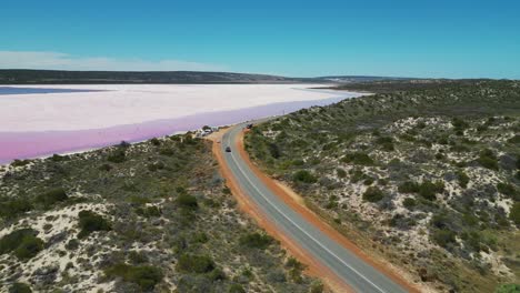 aerial of car driving a road next to pink hutt lagoon in western australia