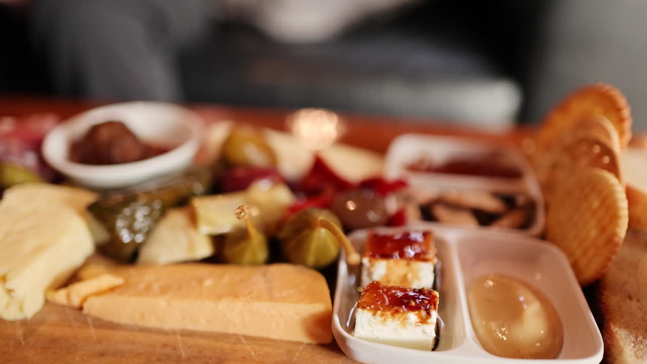 Hand places meatball onto appetizer platter with cheese, crackers, pickles, and antipasto. Shallow focus