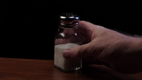 male hand picks up a salt shaker off of a table