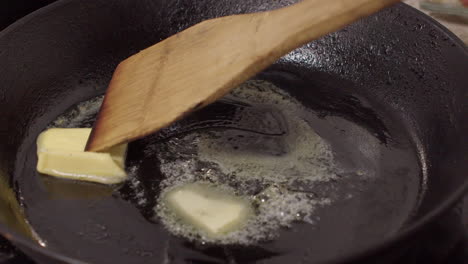 wooden spatula stirs melting butter in hot cast iron pan to coat base