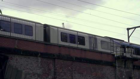 Train-passing-by-on-track-on-bridge-above-road,-level-with-treetops-1