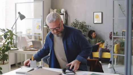 Senior-Man-Walking-in-Call-Center-Office-and-Sitting-at-Workplace