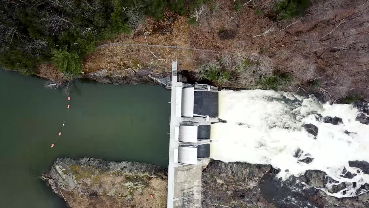 Aerial view over dam spillways during springtime, with a large volume of water flowing over the rocks.