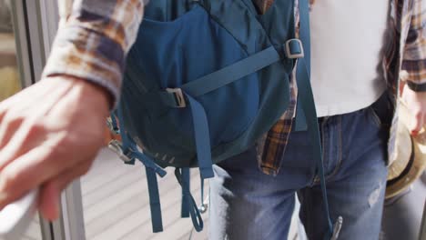 Diverse-couple-walking-with-baggage-and-hats-and-opening-door