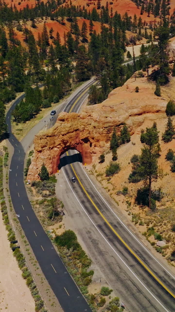 Rocky arch over the motorway in National park in United States. Bright sunny day in Arches Canyons, Utah. Aerial view. Vertical video