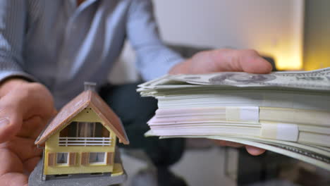 close up shot of adult man lifts house or money stack at home - consideration of cash money or estate investment