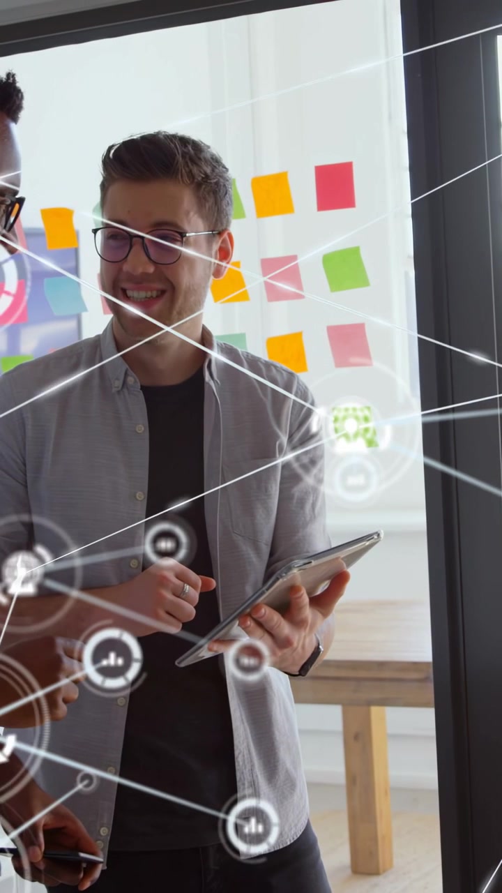 Vertical video: Pair teaming tapping tablet initiating tech HUD mapping links over glass wall notes