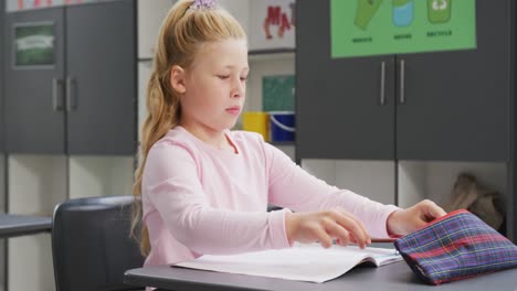 video portrait of caucasian schoolgirl sitting at desk in school class, with copy space