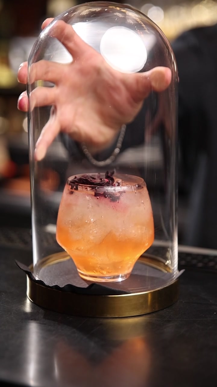 Barman che affumica un cocktail artigianale sotto una cloche di vetro