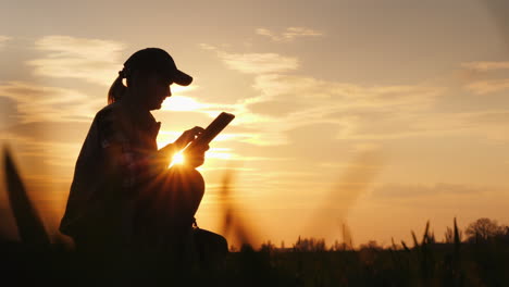 Young-Woman-Farmer-Studying-The-Seedlings-Of-A-Plant-In-A-Field-Using-A-Tablet