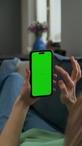 woman using smartphone with green screen on couch