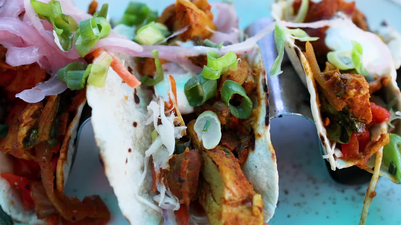 A detailed view of colorful tacos filled with meat, topped with onions and greens on a blue plate.