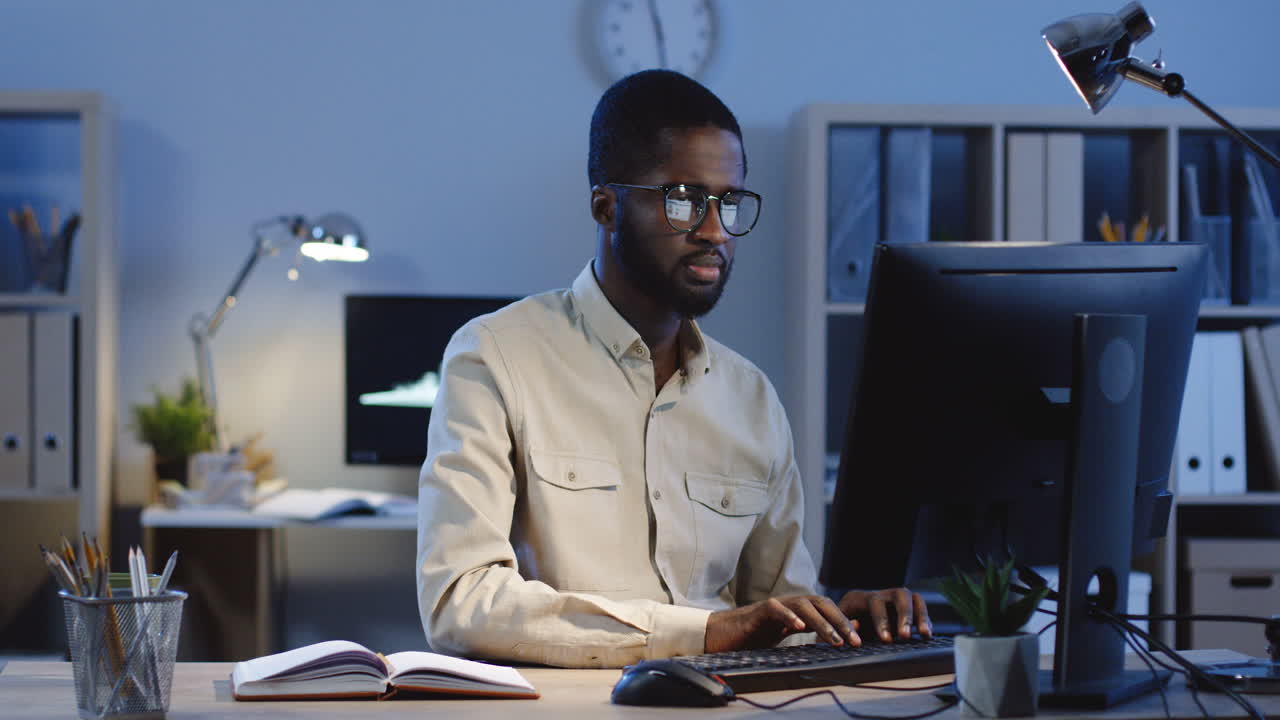 Young Man Working On The Computer When Getting A Message On His Smartphone And It Cheering Him Up