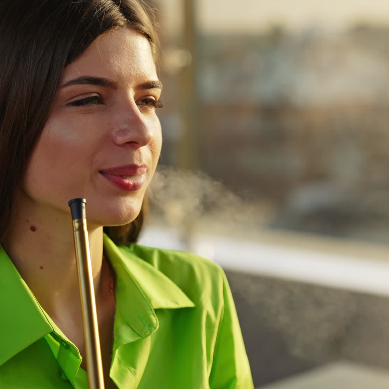 Dark-haired beautiful young lady in green shirt smoking hookah. Relaxing time with nargileh outdoors in summer