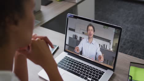 Back-view-of-african-american-woman-having-a-video-call-with-male-colleague-on-laptop-at-office