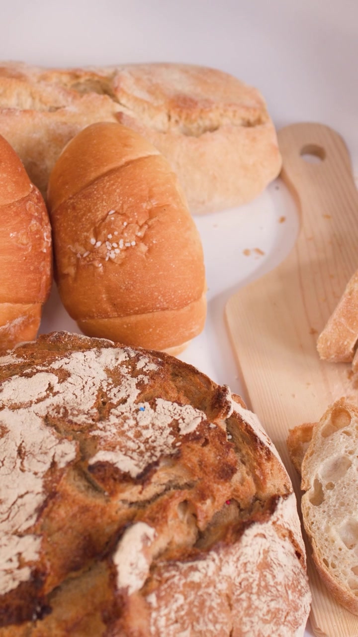 Hands slice crusty baguette on wooden board surrounded by sourdough loaves and croissants.
