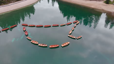 Aerial-forward-shot-from-a-drone-over-aligned-boats-in-Braies-lake-in-the-Dolomites,-Italy