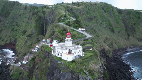 Aerial-drone-fly-green-cliff-lighthouse,-Farol-do-Arnel-in-Azores,-Portugal-Sea