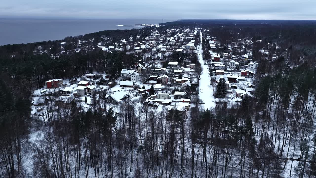 Drone trækker sig tilbage over snedækket by og afslører hovedgade, hav og skov