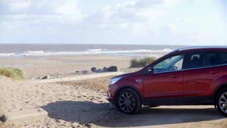 red suv car parked at the beach on the sand next to the ocean