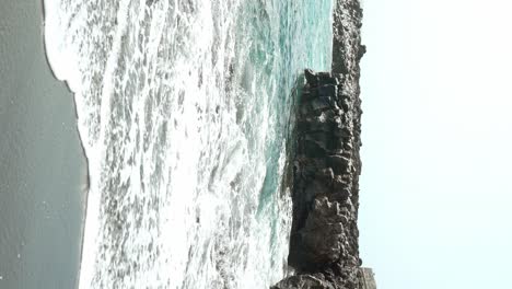 las olas golpean la playa de arena volcánica negra en tenerife, vista vertical