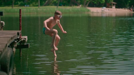 caucasian kid jumping from the wooden pier into the lake