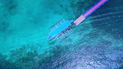 Spectacular 4K overhead drone shot of a traditional outrigger boat moored to a floating dock over crystal-clear turquoise waters in Boracay, Philippines
