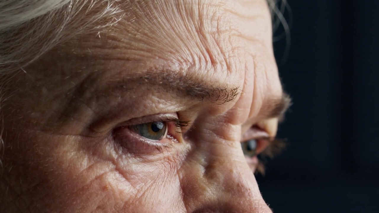 Opening senior woman eyes in studio, soft left lighting causing slow blinks and revealing wrinkles